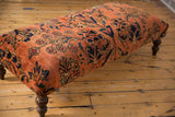 Lilihan rug ottoman corner; dusty rose, navy floral pattern, aged texture, curved wooden leg.
