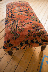 Close-up of hand-knotted vintage Lilihan rug ottoman, dusty rose with navy and gold floral motifs.