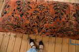 Vintage Lilihan rug ottoman, dusty rose floral pattern, visible wear and person's feet.