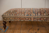 Vintage Persian rug ottoman side, featuring intricate geometric border and rich, turned wooden leg.