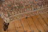Close-up of vintage Persian rug ottoman corner, muted rust, beige, blue traditional pattern, dark wood leg.
