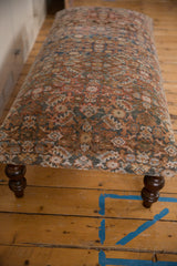 Vintage Persian rug fragment upholstery with intricate rust, blue, beige patterns and a dark turned leg.