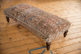 Corner view of the ottoman, highlighting its muted vintage Persian rug pattern and dark turned leg.