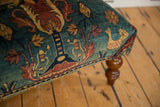 Antique rug ottoman corner with a visible chicken motif and a polished turned wooden leg.