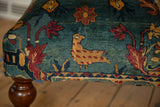 Corner detail of a reclaimed rug ottoman showing a pictorial chicken motif on a sapphire blue field.
