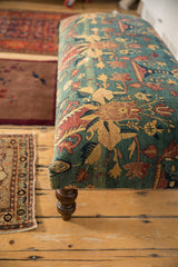 Detailed corner of an antique rug ottoman showing the floral textile and a turned wooden leg.