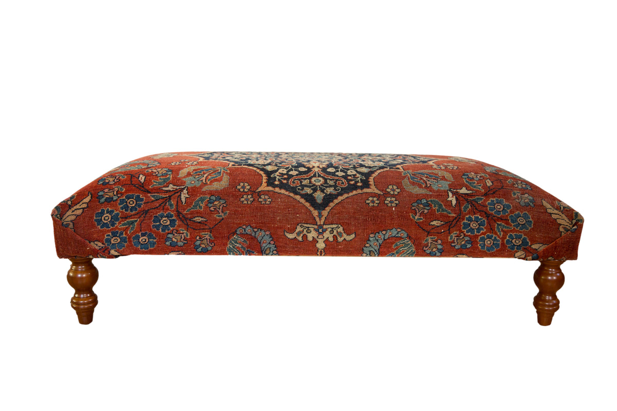 Antique Persian rug ottoman in cochineal red and dark navy blue with floral motifs on turned wood legs.