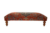 Antique Persian rug ottoman in cochineal red and dark navy blue with floral motifs on turned wood legs.
