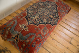 Angled view of the antique Persian rug ottoman, highlighting the navy medallion and cochineal red field.