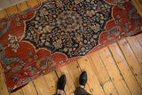 Overhead view of an antique Persian rug ottoman showing its floral pattern in cochineal red and dark navy blue.