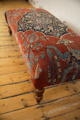 Antique Persian rug ottoman corner detail with red floral textile and a turned wood leg.