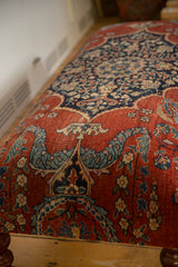 Close-up of an antique rug ottoman showing cochineal red and navy blue floral upholstery details.