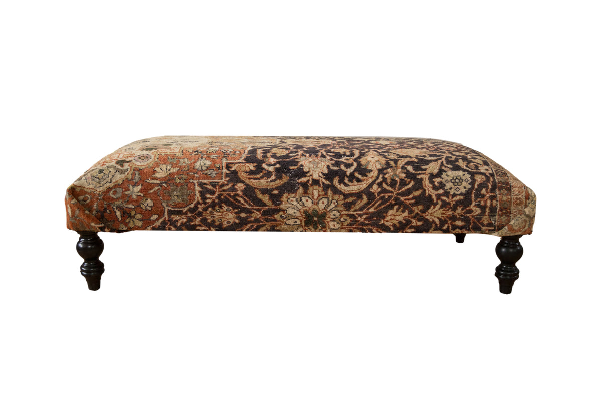 Vintage Persian rug ottoman with charcoal and terracotta floral upholstery and dark turned legs.