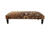 Vintage Persian rug ottoman with charcoal and terracotta floral upholstery and dark turned legs.