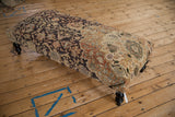 Angled view of the vintage rug ottoman, highlighting the contrast between its dark charcoal and lighter terracotta sections.