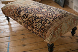 Angled view of the vintage rug ottoman showing the charcoal and terracotta floral pattern.