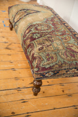 Antique Kerman rug ottoman with sand, pistachio, and aubergine curvilinear motifs; dark turned leg.