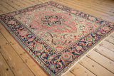 Vintage Heriz rug from an angle, showing its ruby field, central medallion, and wide navy border.