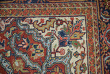 Heriz carpet corner with bold geometric and scalloped motifs in brick red, navy, and ivory.