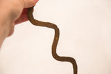 Wavy vintage iron snake held by hand, showing its rustic, rust-brown texture.