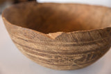 Hand-carved texture and prominent chip on the rim of a vintage African wooden bowl.