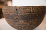 Close-up of dark primitive wooden bowl, showing carved geometric bands and prominent wire repair.