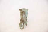 Rear view of a vintage copper animal figure, showing its curled tail and mottled green patina.