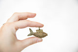Hand holding the vintage bronze fish pendant to show its handmade texture and scale.