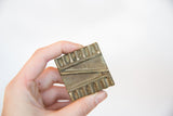 Vintage square bronze coin held to display its rustic texture and scale.