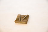 Angled view of a vintage square bronze coin with a raised geometric V-pattern and ridges.