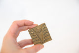Vintage African square bronze coin held to show its handmade, stamped details.