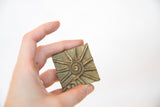A hand holds the vintage square bronze coin, showing its size and sun pattern.
