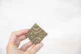 Vintage African bronze coin, handheld, with an intricate wavy pattern and aged patina.
