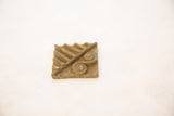 Textured surface of a vintage square bronze coin with raised spiral motifs.