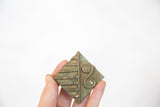 A hand holds the square bronze coin, showing its aged patina and incised patterns.