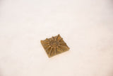 Vintage square bronze coin with a central spiral sun motif and rustic texture.