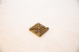 Side angle of a square African bronze coin showing the depth of its raised patterns.
