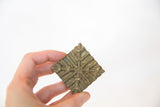 A hand holding the vintage African bronze coin to show its scale and geometric texture.