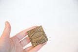 Vintage African bronze coin with a raised pattern held in hand to show scale.