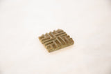 Angled view of a square bronze coin highlighting its textured, raised interwoven design.