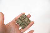 A hand holding the vintage square bronze coin, showing its scale and geometric stamp design.