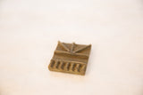 Angled view of a vintage square bronze coin showing its raised geometric pattern.