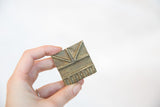 Vintage African bronze coin with handmade geometric patterns held for scale.
