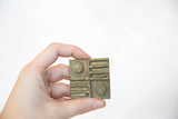 Square vintage African bronze coin with detailed raised pattern and patina.