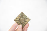 Vintage African square bronze coin held in hand, revealing its textured starburst pattern.