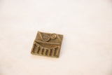 The rustic texture and aged patina of a square African bronze coin with embossed spirals.