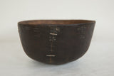 Side view of vintage African wooden bowl, highlighting etched waves and metal staple repairs.