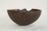 Aged dark brown African wooden bowl displaying rugged texture and visible rim repairs.
