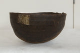 Aged African wooden bowl with dark textured surface and metal repair patch.
