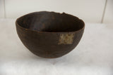 Dark brown vintage African wooden bowl with rustic metal patch and visible cracks.